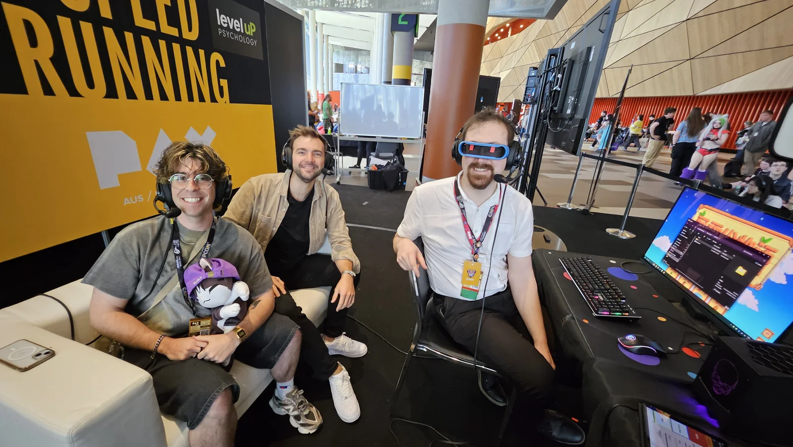Three participants wearing headsets at the PAX Aus speedrunning area, seated beside a gaming setup.