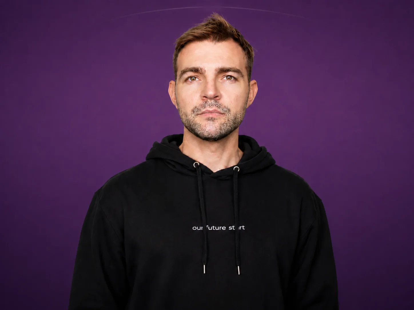 Portrait of Seb Fehr wearing a black hoodie against a purple background.